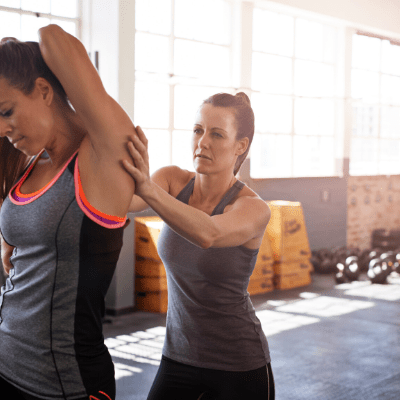 Female trainer helps female client stretch in the gym